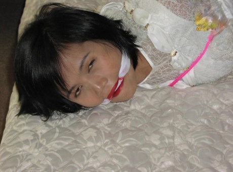 Asian girl is cleaved gagged while tied up in her clothing on a bed