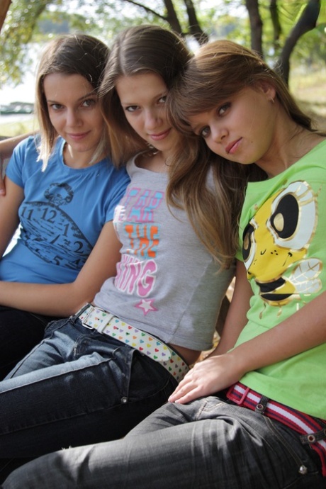 Tři mladé dívky si svléknou trička a džíny a modelují nahé na lavičce v parku