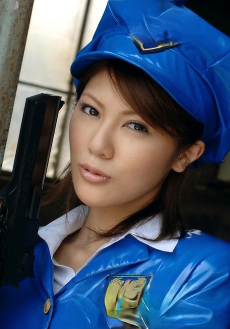 Anna, policière asiatique, manie un pistolet en jupe courte en latex et en collants.
