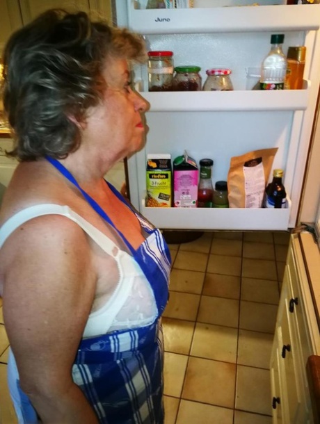 Die alte Hausfrau Caro zieht ihre Unterwäsche in Küchenschürze und Strümpfen aus