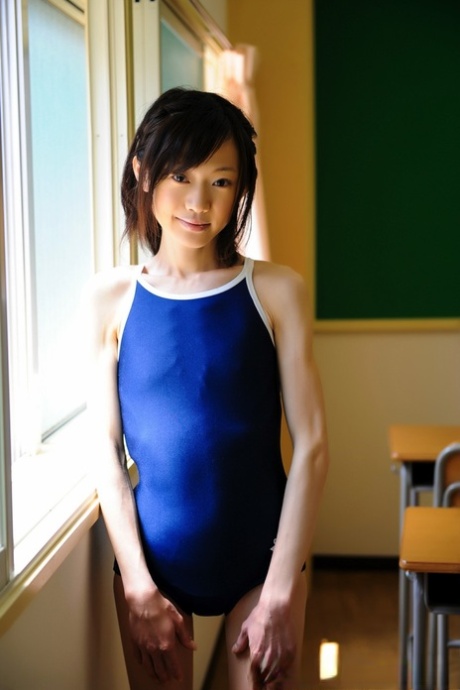 Winziges japanisches Mädchenmodell nicht nackt in einem Badeanzug auf Schulbank
