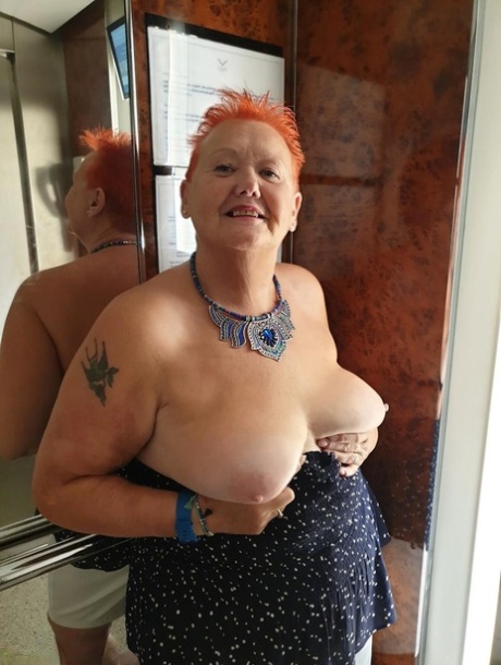 Fat nan with short red hair presses her big boobs and butt up against glass
