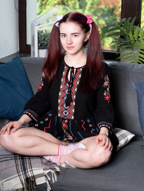 Junger Teenager Polina zieht sich auf einem Sofa in Zöpfen bis auf die Socken aus