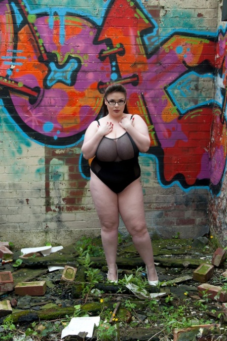 Den brune fede Gina G viser sine bryster, mens hun er nøgen nær graffiti