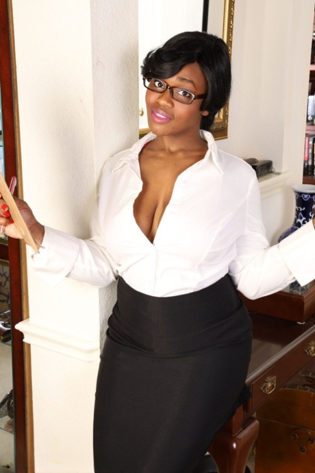 Una mujer negra de más de 30 años, Sunny, se quita la ropa de negocios para modelar desnuda con tacones y gafas