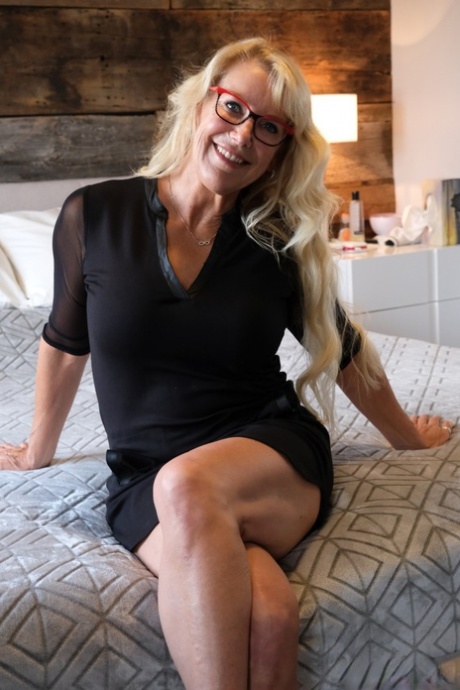 Busty blonde doffs her clothes and glasses before sex on a bed