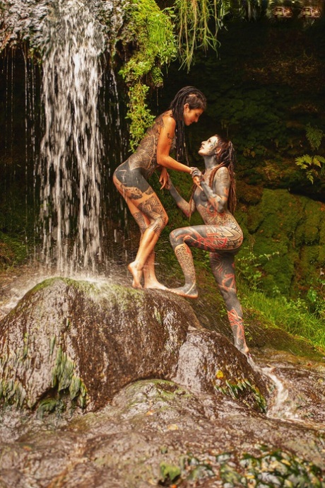 Heavily tattooed lesbians hold each other while totally naked on a bridge