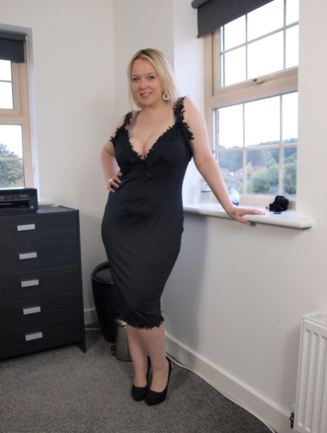 Die übergewichtige britische Blondine Sindy Bust zieht ein schwarzes Kleid aus, um sich auf einem Bett auszuziehen