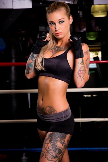 La MILF tatouée Kleio Valentien en short montrant ses gros seins dans une salle de gym.