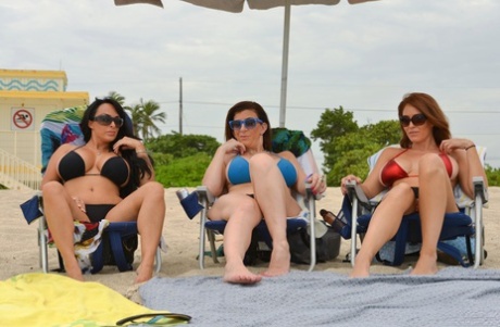 Drie rondborstige strand babes trekken bikinitopjes opzij om te pronken met grote tieten bij het water