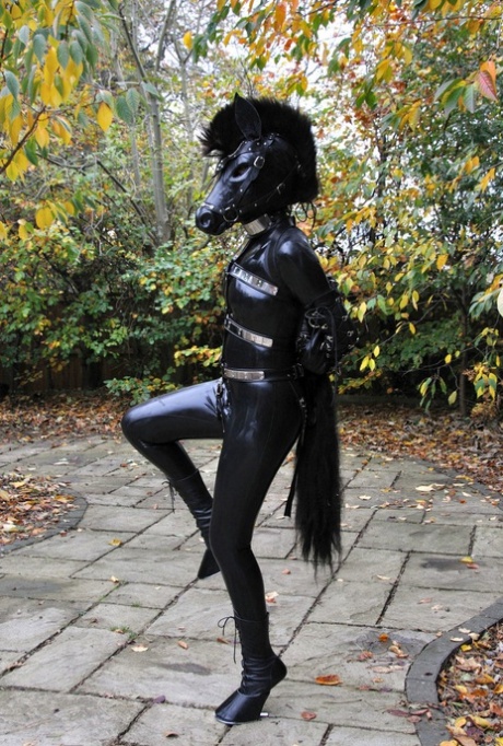 Kinky Schlampe posiert im Freien in einer Pferdemaske und einem vollbedeckenden Latex-Outfit