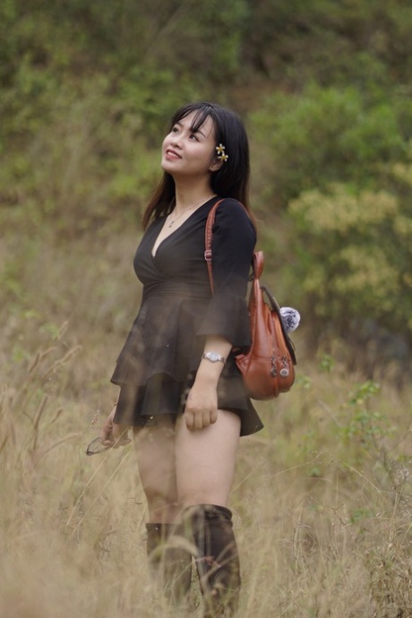 Gorgeous Asian babe posing in her black dress and boots in nature